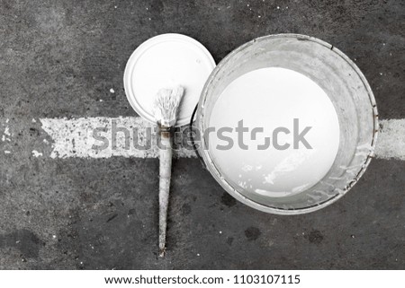 Brush and bucket with white paint on a white line