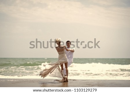 Prelude - couple in love. Pretty happy young wedding couple of boy and girl in white spinning on ocean beach coast on windy weather sunny day outdoor on blue sky background, horizontal picture