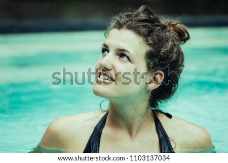 Closeup of smiling young woman looking away and swimming in pool. Front view.