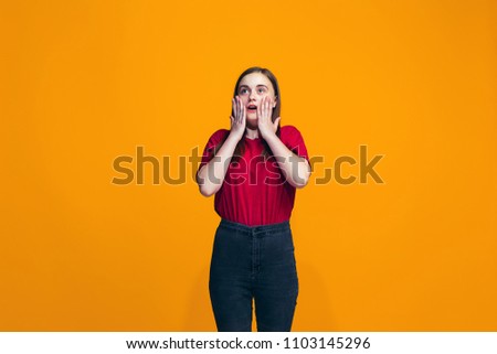 Wow. Beautiful female half-length front portrait isolated on orange studio backgroud. Young emotional surprised teen girl standing with open mouth. Human emotions, facial expression concept. Trendy