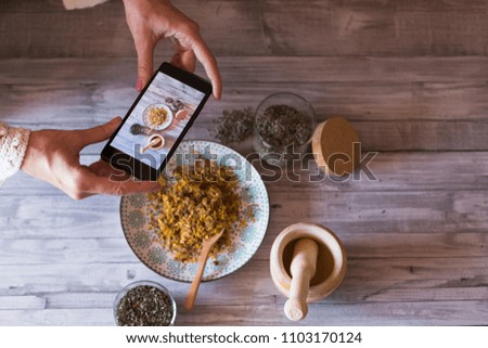 Young woman food blogger takes photo for blog, pic of a wooden mortar, bowl with yellow turmeric, lavender and healthy natural ingredients. Selective focus, closeup. Daytime