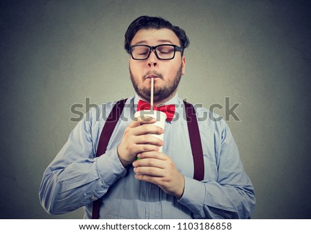 Young bearded man with overweight holding eyes closed and drinking sweet soda with deep enjoyment Royalty-Free Stock Photo #1103186858