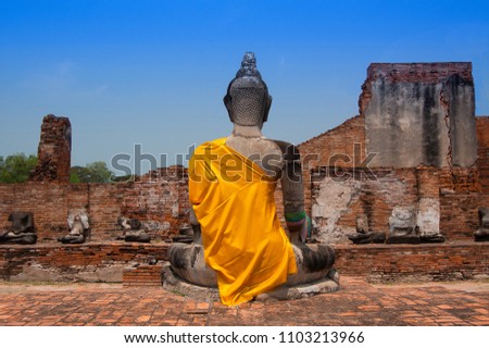 Backside of outdoor old buddha statue in Ayutthaya, Thailand, which are dressed in yellow robe. The background are broken brick wall and vivid blue sky. Photo by aleksolo