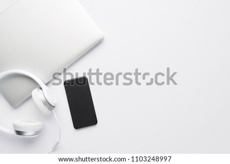 Minimal work space concept. Top view of laptop, white headphones and black cell phone on white background with copy space. Flat lay.