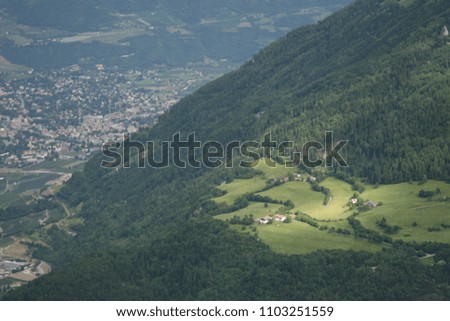 Landscape in alps with mountains view, snow tops, pines and christmas trees forest, green grass meadows, dramatic blue pink grey sky, sun rays and cozy wooden houses on mountainsides  