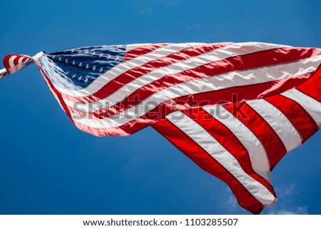 American flag flying on a flagpole blowing in the wind on a beautiful windy day