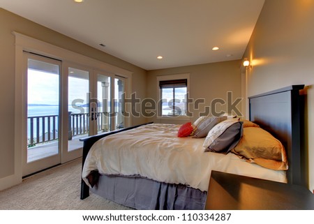 Bedroom with water view, queen bed and beige walls.