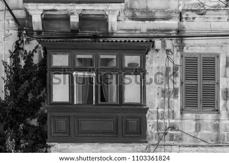Building with traditional maltese window decorated with fresh flowers. Black and white picture 