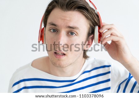 Misunderstanding man not listening in headphones. Confused young guy removing headphones from ear and looking at camera. Do not care concept