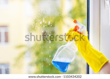 women's hands in bright yellow rubber gloves wash windows with a Pulverizer and a sprayer for washing windows