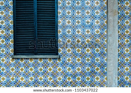 Building wall decorated old ceramic tile. Closed window with wooden jalousie.  Royalty-Free Stock Photo #1103437022
