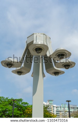 Closeup 360-degree CCTV camera in public area of city with park and cloudy sky background, cluster of security camera in shape of arms of octupus, concept of city safety and security monitoring system