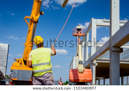 Worker is helping crane from the ground, keep balance and direction. Rigger is helping mobile crane with rope to manage concrete joist for assembly huge construction.