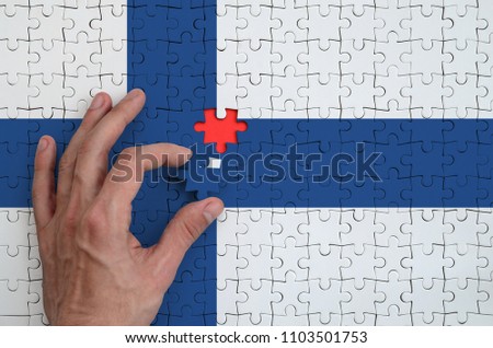 Finland flag  is depicted on a puzzle, which the man's hand completes to fold