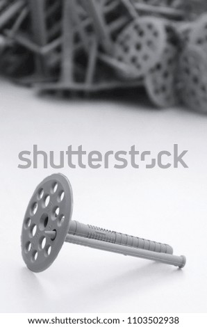 A gray plastic dowel fastening for thermal insulation with round umbrella caps lies on a gray foam polystyrene plate