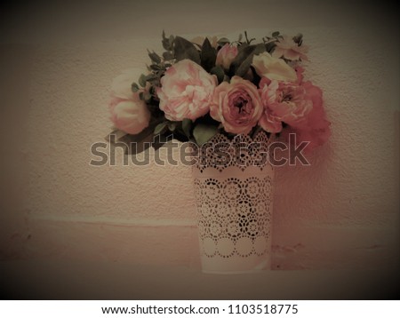Bouquet of flowers with roses, in a vase with a paper cuff, arranged in front of a pink environment, the picture is exposed and developed in the style of a paper photo from the 1950s.