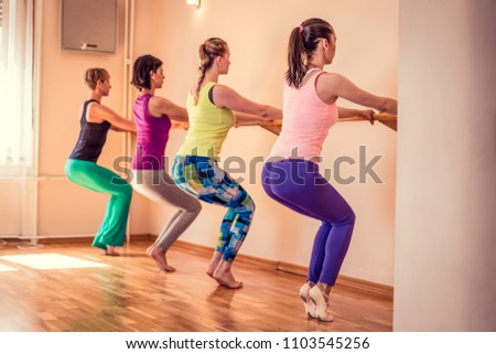 Beautiful adult women doing exercises on stretching ballet bar in Pilates class. Group of females doing yoga, pilates and fitness exercise indoors in studio. Royalty-Free Stock Photo #1103545256