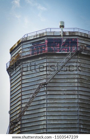 Round metal tower. Old industrial construction with painted letters, tank system with ladder. Cities and urban life concept photo