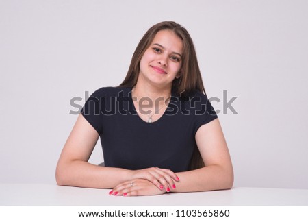 I listen carefully to you. Portrait of a beautiful manager girl on white background at a table. She sits right in front of the camera smiling and looks happy
