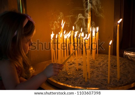 Little girl prays and puts a candle in the Orthodox Church