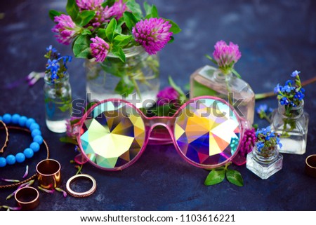 Stylish pink kaleidoscopic sunglasses with golden bracelets and rings in a feminine style concept with clover flowers on a dark background. Beautiful summer accessories.