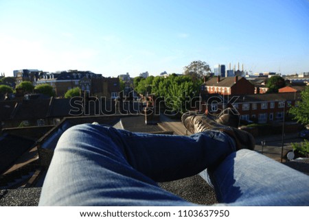 POV image of legs as the photographer sits on a rooftop in a city looking out towards the other buildings.
