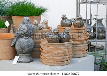 Stone and ceramic birds, green grass in flower pots and old dishes in a flower shop