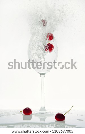 Red flying cherries pop out of a glass with sparkling water