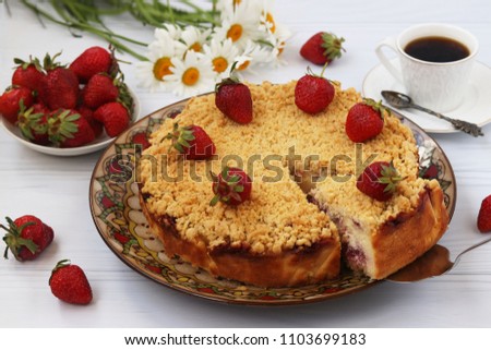 Curd cake with strawberries with a cut out piece of cake is located on a white background. Also in the picture there is a cup of coffee, a bowl of strawberries and a bouquet of chamomiles.