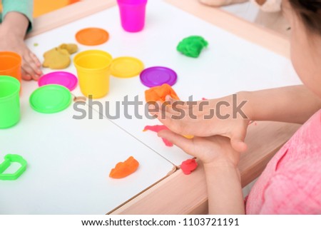 Cute little girl using play dough at table, closeup