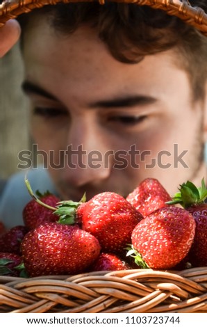 
blurred image, selective focus. a young man eats a strawberry with pleasure. holds a basket with a berry