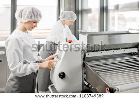 Women in uniform working with dough rolling machine at the bakery manufacturing