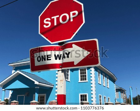 Stop sign and one way sign against blue sky and blue house in Haiti
