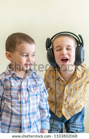 A little boy with his headphones dances with his brother. Two little brothers in shirts amuse themselves and dance.