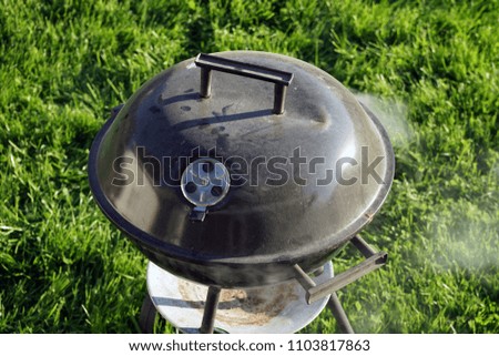 Barbecue grill standing on lawn outdoors in a sunny day. Smoke come out of it, ready for grilling.