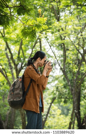 Asian male traveler carried a travel bag and take a photo by camera in the forest. concept of travel, trip