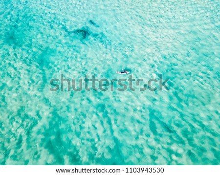 An aerial view of a surfer paddling in blue water at the beach