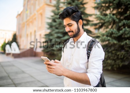 Indian male student texting on smartphone in the street Royalty-Free Stock Photo #1103967800