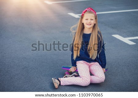 A fashionable little cute girl outdoors with skateboard. Beautiful summer day over urban background