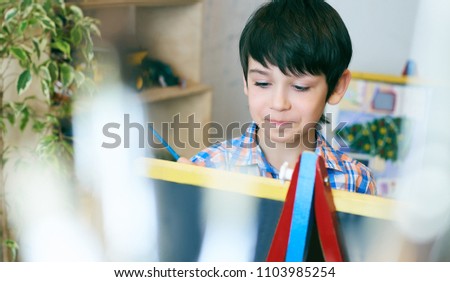 Child standingnext to the easel. Kid boy learn paint by brush in class school. Kindergarten interior on background. Boy is getting ready to become an artist.
