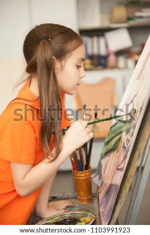 Portrait of a lovely little girl painting a picture in a studio or art school. Creative pensive painter child paints a colorful picture on canvas in workshop. Talented kids.