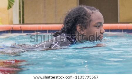 Portrait of African American teenage girl in pool and rain expressions swimming floating having fun