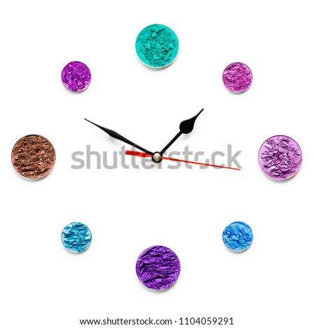 Creative concept photo of cosmetics swatches beauty products round eyeshadow arranged as an alarm clock on white background.