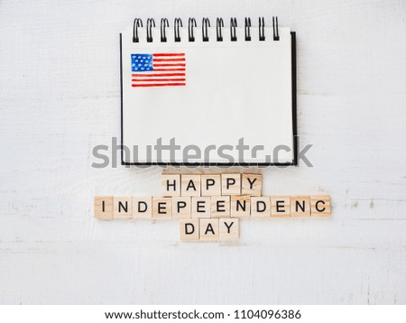 Sketchbook with a picture of the US flag, blank page, wooden letters of the alphabet with congratulations on the US Independence Day on a white, isolated background. Top view, close-up