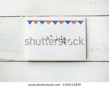 Postcard with a picture of the US Flag and a handwritten inscription 4th July on a white, vintage wooden table. Top view, close-up. Concept of an independent, strong country and nation