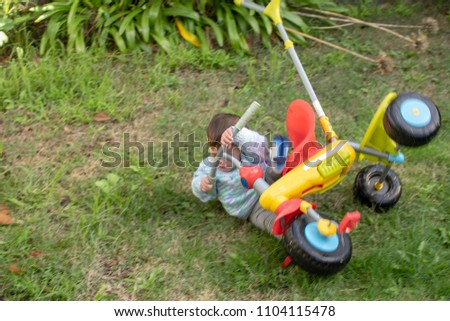 Motion blurred picture, baby is falling off his plastic bicycle when first time try to practice on the grass