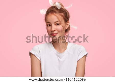 Positive relaxed Caucasian female just awoke, wears casual clothes, stands against pink background, being in good mood, recieves pleasant compliment from husband at morning. Bed time and emotions