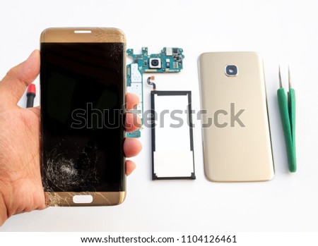 Close-up of cracked smartphone screen in technician hand on blurred smartphone component background
