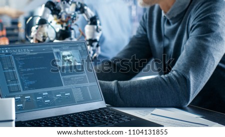 Robotics Engineer Manipulates Voice Controlled Robot, Laptop Screen Shows Speech and Face Recognition Software. In the Background Robotics Reseatch Center Laboratory.