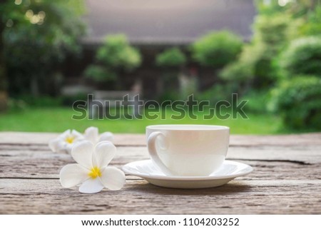 a selective focus picture of a cup of coffee on wooden table with green grass field in the morning sunrise